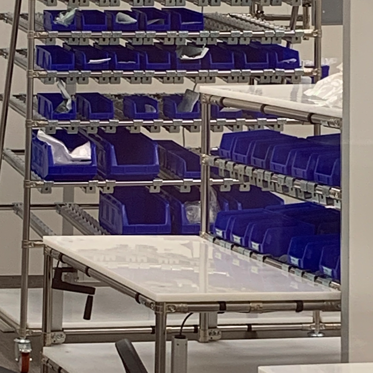 sistema di stoccaggio costituito da una struttura tubolare modulare, probabilmente in acciaio o alluminio, dotata di contenitori blu impilati su più livelli. Questi contenitori sono utilizzati per organizzare piccoli componenti o materiali, rendendo il sistema ideale per ambienti industriali, di assemblaggio o magazzini. La presenza di un piano di lavoro integrato evidenzia un design pensato per ottimizzare spazio e funzionalità operative.